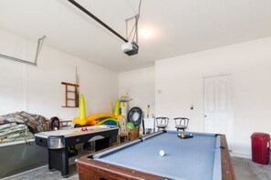 Uma mesa de bilhar com uma bola branca, um projetor fixado no teto e uma porta ao fundo.