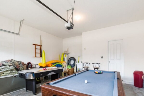 Een pooltafel met een witte bal, een projector bevestigd aan het plafond en een deur op de achtergrond.