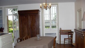 A dining area with a table set for four, wooden chairs, a chandelier, and a view through a window with lace curtains. - Le Champ Bonnot - Rigny-sur-arroux (RIGNY-SUR-ARROUX)