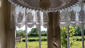 A window with a decorative lace curtain, a metal gate, and a view of a garden. - Le Champ Bonnot - Rigny-sur-arroux (RIGNY-SUR-ARROUX)