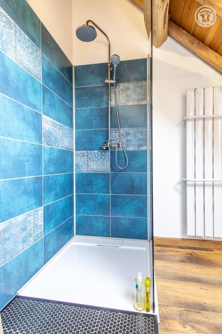 A modern shower with blue tiles and a wooden floor.