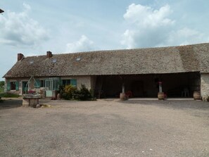 Traditional farmhouse with a large open garage area and dirt floor.