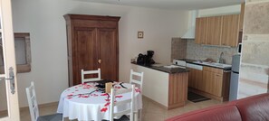 A compact kitchen with wooden cabinets, a dining table with a white tablecloth, and a red sofa in the foreground. - Château de Mouhy - Prisse (PRISSE)