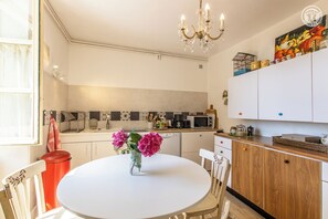 A modern kitchen with white cabinets, a round dining table, and a chandelier. - Aux 3 Marronniers – MERCUREY (MERCUREY)