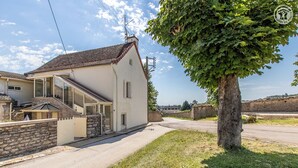 Une maison à deux étages, avec des fondations en pierre, un toit en tuiles et un grand arbre devant.