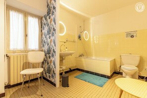 Ein Badezimmer mit Toilette, Waschbecken und Dusche. Es ist ein Stuhl und ein kleiner Tisch vorhanden.