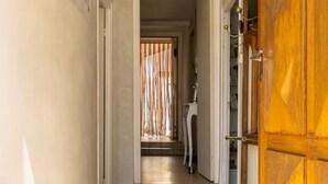 Un couloir doté d’un plancher en bois, une porte en bois sur la droite et, au fond, une vue sur une autre pièce séparée par un rideau.