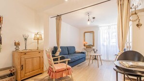 Un salon avec un canapé bleu, un meuble en bois, un fauteuil à carreaux rouges et blancs, une petite table ronde et un lustre.