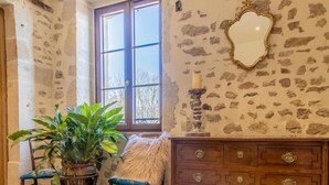 A room with stone walls, a wooden dresser, a mirror, and a window with a view.
