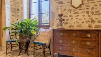 Een kamer met stenen muren, een houten dressoir, een spiegel en een raam met uitzicht.