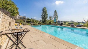 A swimming pool with a wooden deck, lounge chairs, and a stone wall. - Le Puits - Saint Sernin DU Plain (SAINT SERNIN DU PLAIN)