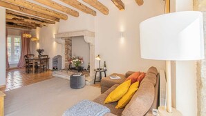 A cozy living room with exposed wooden beams, a fireplace, a dining area, and a sofa with cushions. - Le Puits - Saint Sernin DU Plain (SAINT SERNIN DU PLAIN)