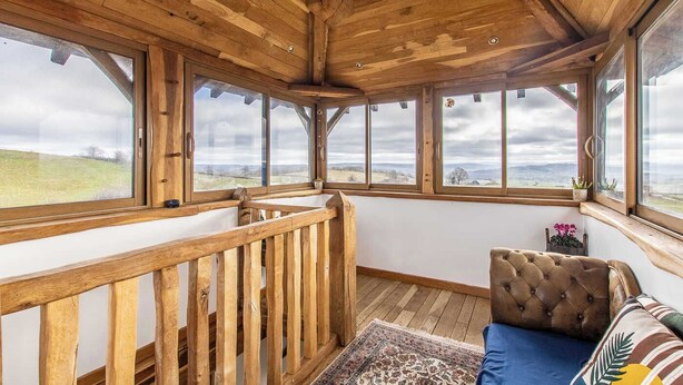 A wooden interior with large windows, a wooden railing, and a tufted sofa.