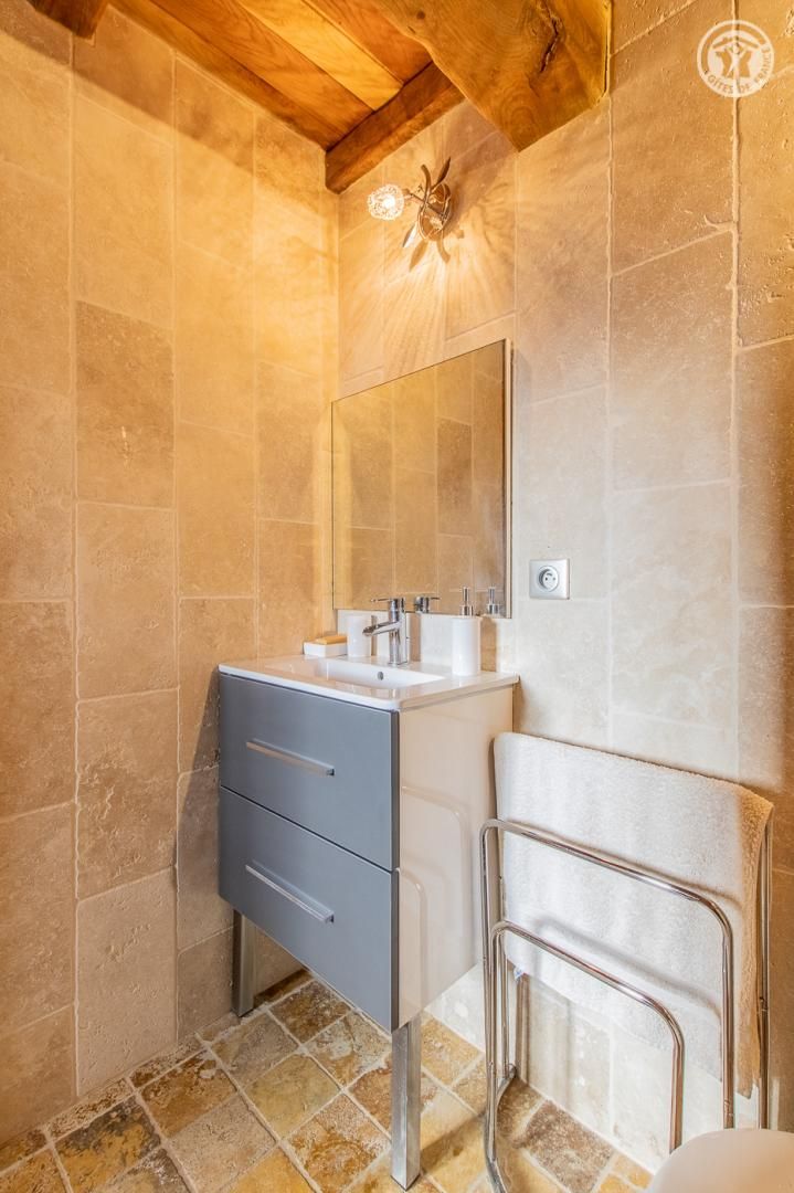 Ett badrum med beige stenkakel, ett träpanelat tak, en modern handfat med spegel och en handdukshängare.