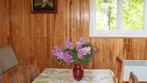 A wooden-paneled room with a table, chairs, a vase of flowers, and a window with a view of greenery.