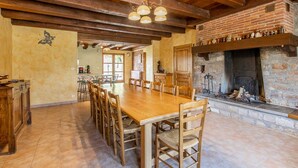 Un comedor amplio con una larga mesa de madera y sillas, una chimenea de ladrillo y un techo de madera con vigas a la vista.
