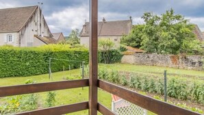 A covered patio with a wooden ceiling and metal railing, overlooking a garden with a hedge and a stone wall. - Au Fil de la Cozanne (PARIS L'HOPITAL)