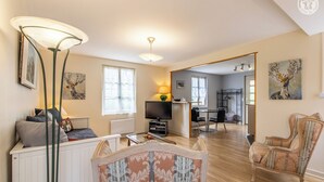 A modern living room with a sofa, a coffee table, and a TV. There is a dining area with a table and chairs. - Au Fil de la Cozanne (PARIS L'HOPITAL)