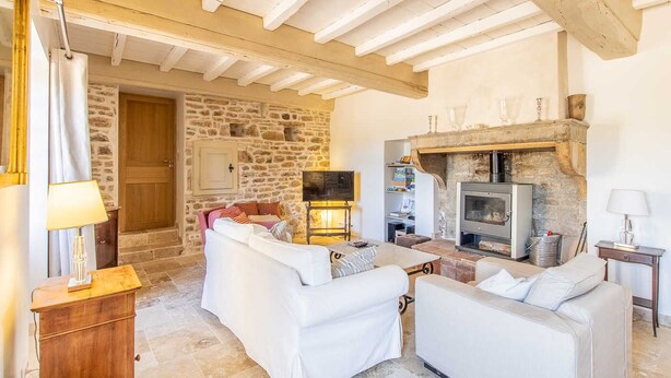 Una sala de estar acogedora con pared de piedra, chimenea y muebles blancos.