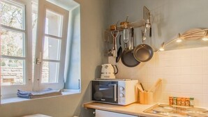 A compact kitchen with a window, a microwave, a stove, and hanging pots. - Maison du Mont Rome - Saint Sernin DU Plain (SAINT SERNIN DU PLAIN)