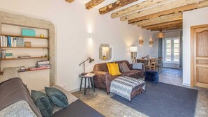A cozy living room with exposed wooden beams, a brown sofa with yellow pillows, a patterned ottoman, and a bookshelf filled with books. - Maison du Mont Rome - Saint Sernin DU Plain (SAINT SERNIN DU PLAIN)