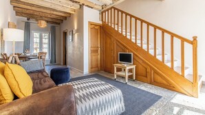 A cozy living room with a wooden staircase, a TV on a small table, and a sofa with cushions. - Maison du Mont Rome - Saint Sernin DU Plain (SAINT SERNIN DU PLAIN)