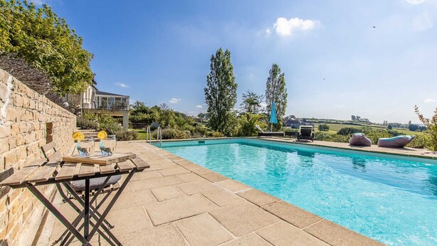 A swimming pool with a wooden deck, lounge chairs, and a stone wall. - Maison du Mont Rome - Saint Sernin DU Plain (SAINT SERNIN DU PLAIN)