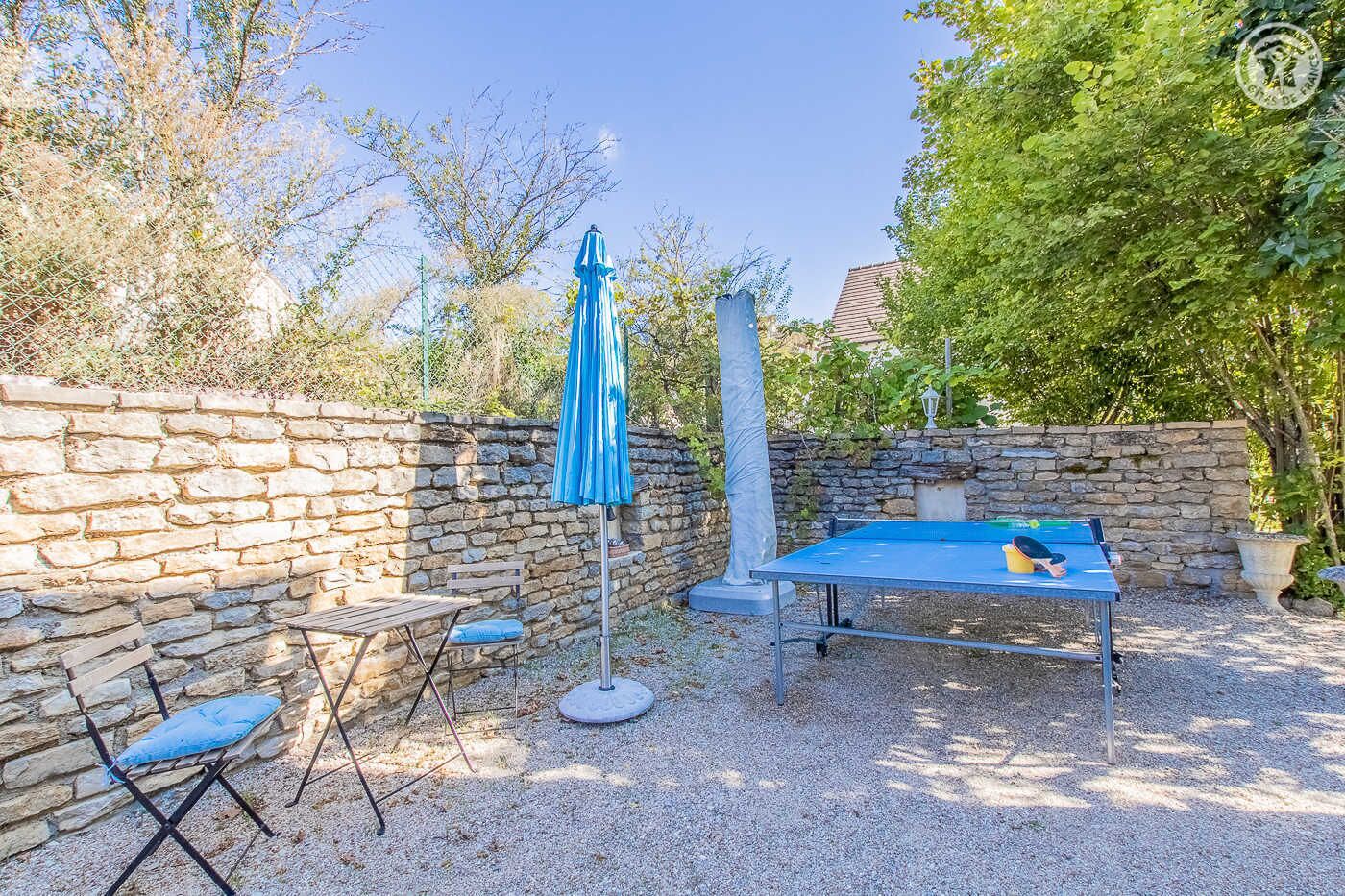 Une table de billard recouverte d’une nappe bleue, un parasol bleu et un mur de pierres, le tout dans un cadre de jardin.
