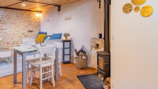 A cozy room with a wooden floor, a stone wall, a dining table with chairs, a sofa, a fireplace, and a loft area with a wooden ceiling. - Mezzabulle - Chapaize (CHAPAIZE)