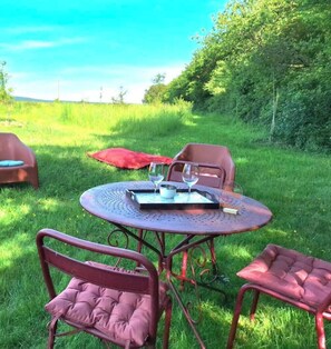 Een ronde metalen tafel met twee glazen en een dienblad, omringd door rode, beklede stoelen in een gazon.