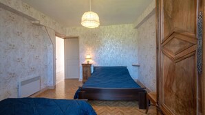 A bedroom with a bed, a nightstand with a lamp, a radiator, and a wooden wardrobe. - Le Chevalier - Saint-sernin-du-plain (SAINT-SERNIN-DU-PLAIN)