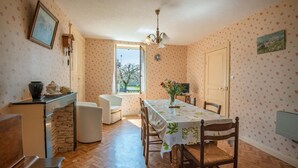 A dining area with a table, chairs, a chandelier, and a window with a view of trees. - Le Chevalier - Saint-sernin-du-plain (SAINT-SERNIN-DU-PLAIN)