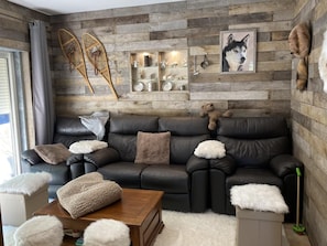 Een moderne woonkamer met een leren bank, een salontafel en een houten wand met planken waarop verschillende objecten staan.