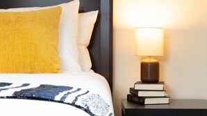 A neatly made bed with a patterned blanket, a yellow pillow, and a white pillow. There is a bedside table with a lamp and a stack of books. - Charming 2 bedroom 2 bathroom home with jetted tub! (Plains)