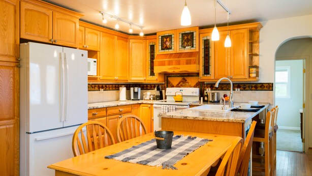 A kitchen with wooden cabinets, a white refrigerator, a stove, and a dining table with chairs. - Charming 2 bedroom 2 bathroom home with jetted tub! (Plains)