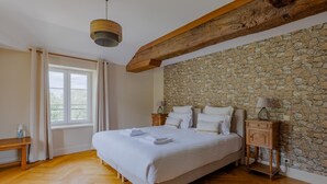A bedroom with a large bed, wooden headboard, stone wall, and a wooden bench by the window.