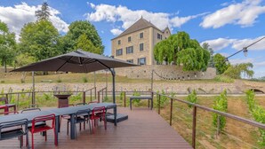 An outdoor patio with tables and chairs, a stone building in the background, and a stone wall with a bridge.