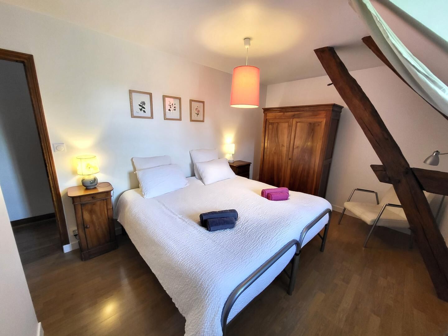 A bedroom with a bed, bedside lamps, a wooden wardrobe, and a sloped ceiling.