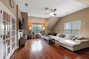 Relax in this spacious living room with a large sofa set and coffee table, featuring a ceiling fan and a window with blinds.