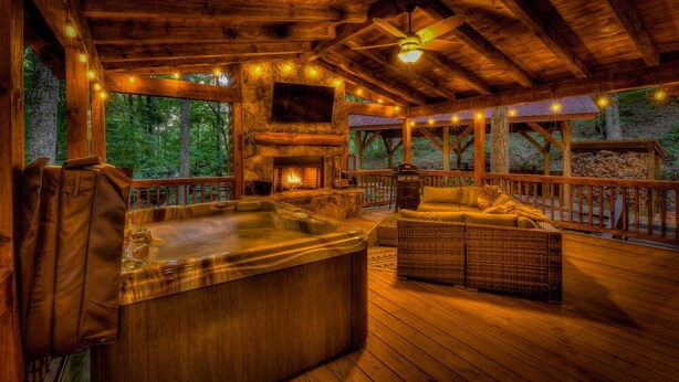 Une terrasse en bois avec un jacuzzi, des meubles en osier et une cheminée en pierre.