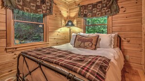 Une chambre dans une cabane en bois, avec un lit, une lampe et des fenêtres donnant sur une forêt.