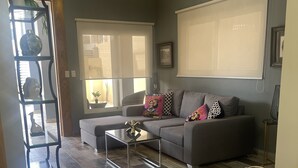 A living room with a grey sofa, a glass coffee table, and a chandelier.