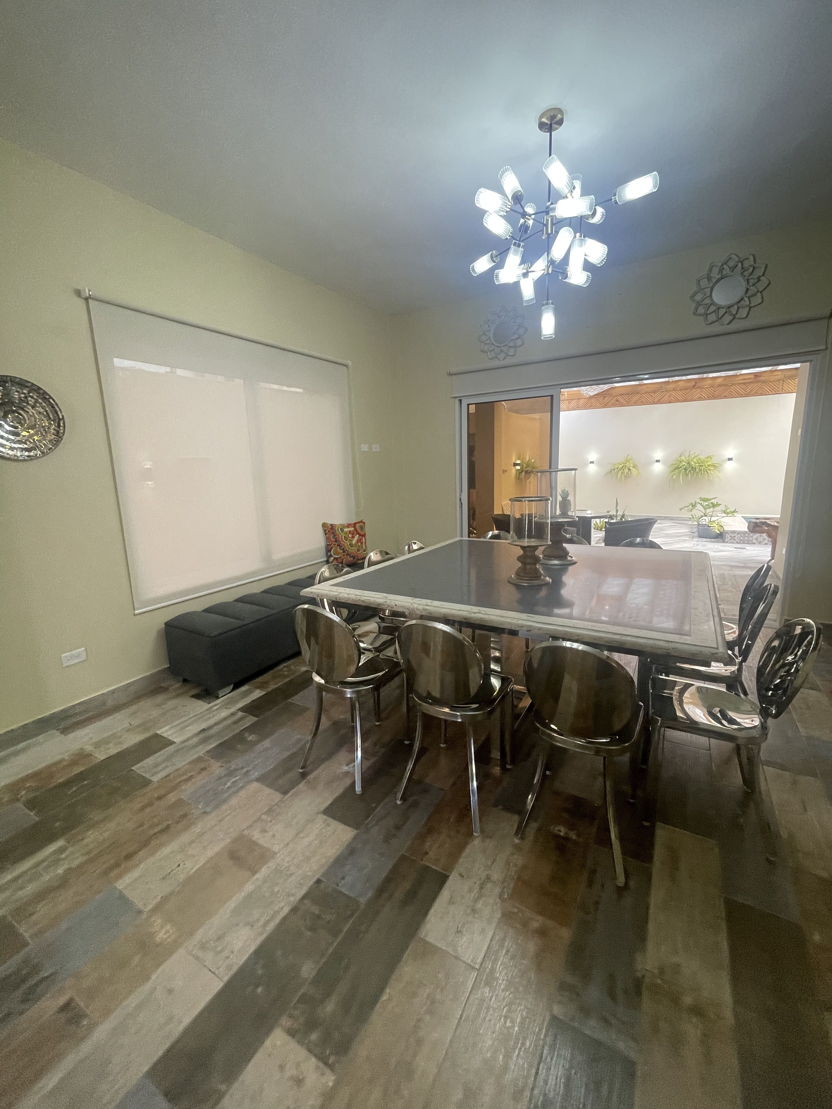 A dining area with a large table and six chairs, a ceiling fan, and a view of an outdoor patio with plants.