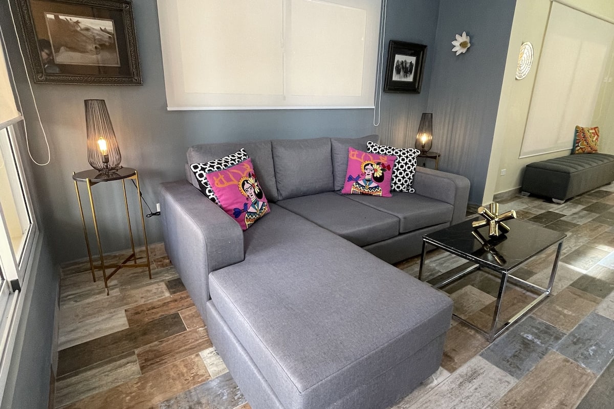 A modern living room with a grey sectional sofa, a glass coffee table, and patterned cushions.