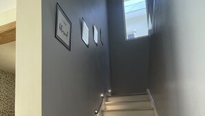 A staircase with a light gray wall, a small window, and three framed pictures on the wall.