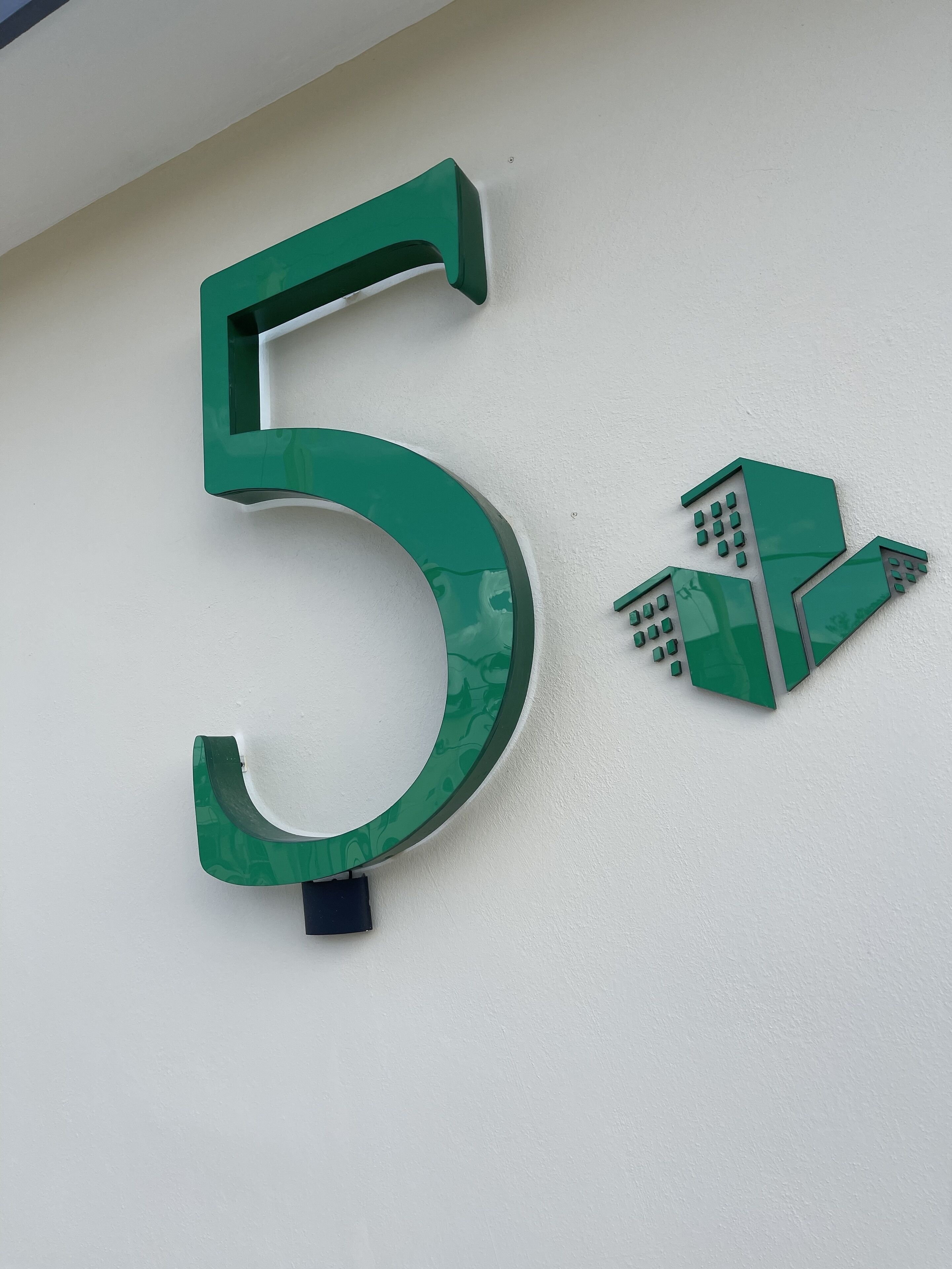 Un grand panneau vert avec le chiffre « 5 » et un petit symbole représentant un bâtiment sur la droite.
