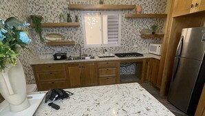 A kitchen with a marble countertop, wooden cabinets, a stainless steel refrigerator, and a tiled backsplash.
