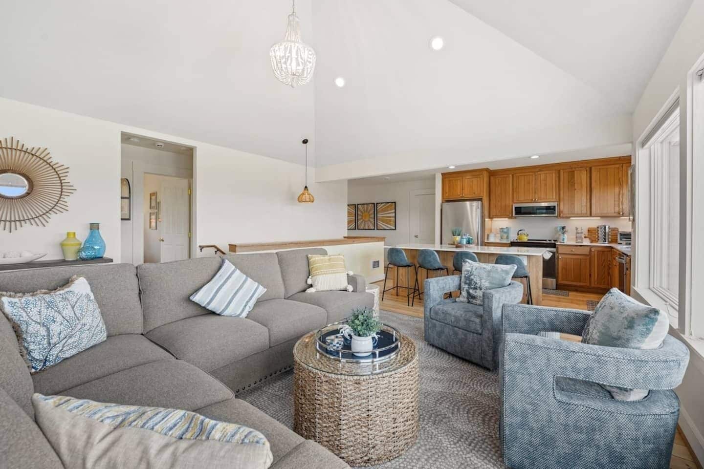 A modern living room with a grey sectional sofa, a round coffee table, and a dining area with bar stools.