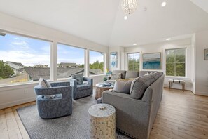 A spacious living room with large windows, a grey sofa, two armchairs, and a round coffee table.