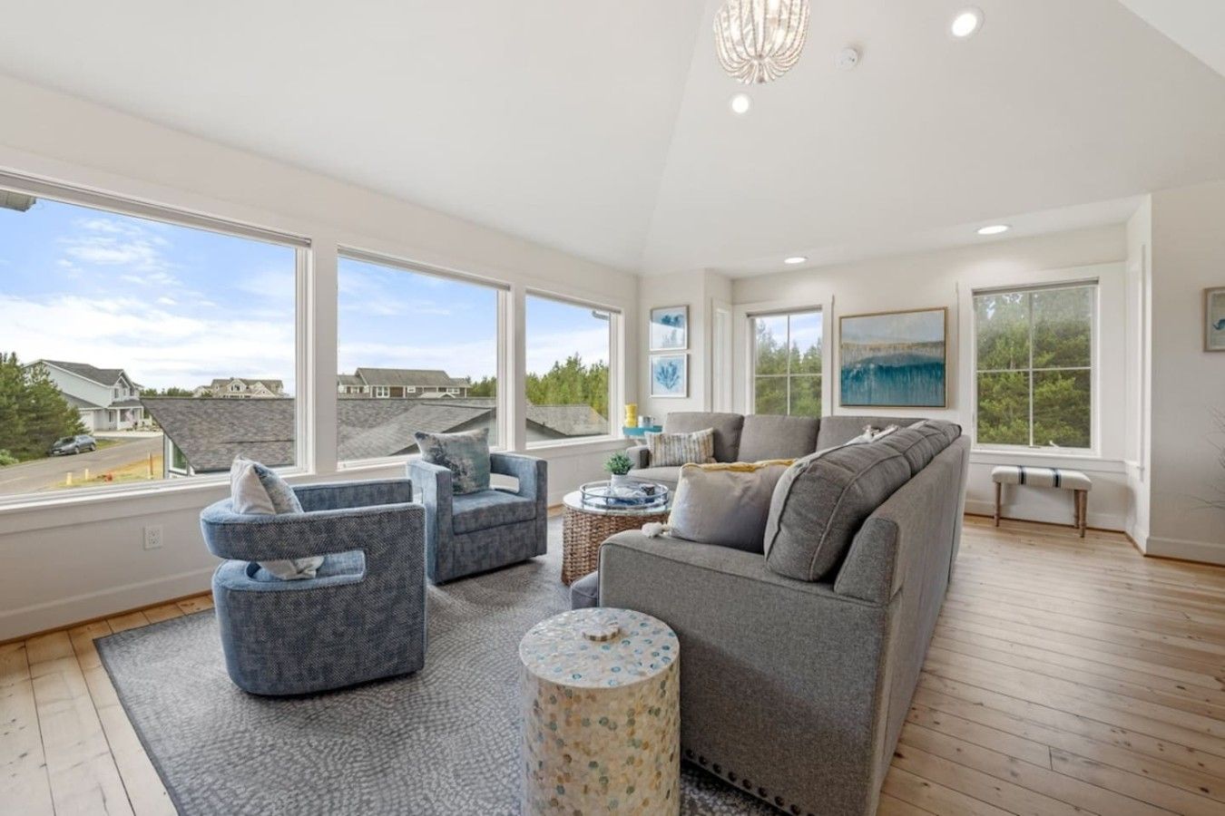 A spacious living room with large windows, a grey sofa, two armchairs, and a round coffee table.